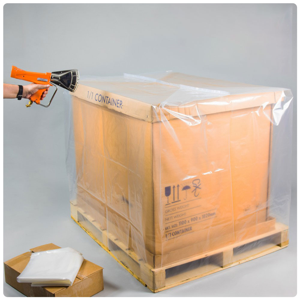 Cardboard box on a pallet with clear plastic wrap and a hand holding a tool.